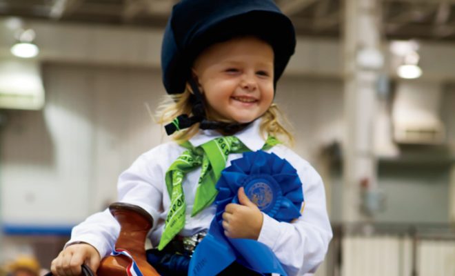 little girl on horse holding blue ribbon at 4-H fair