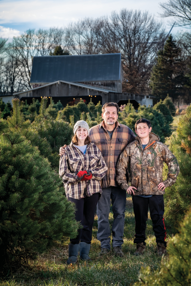 Brian Helmig stands among some Christmas trees with his daughter Isabella and son Aidan at Helmig's Tree Farm