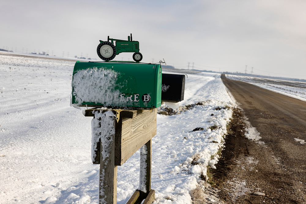 Green mailbox with a decorative tractor on top dusted in snow 