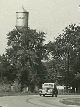 Car on a road with water tower in background, circa 1945