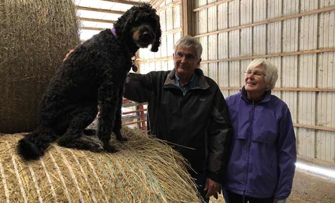 Sandy and John Brix with Bernice who is sitting on top of a round hay bale