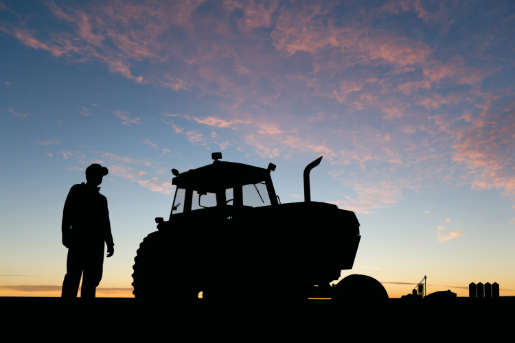 Silhouette of a farmer and tractor at sunset with a barn in the background