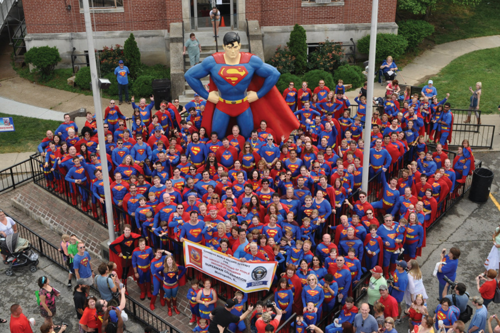 People in Superman attire standing in front of the large Superman statue 