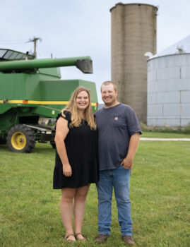 Nathan and Ali Gibbs standing in front of the silo and farm equipment