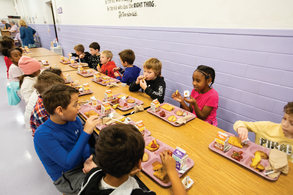 Elementary-age kids sitting at a long table eating lunch in the cafeteria