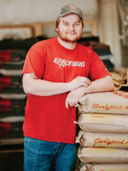Justin Coker leaning on bags of feed with Earlybird packaging
