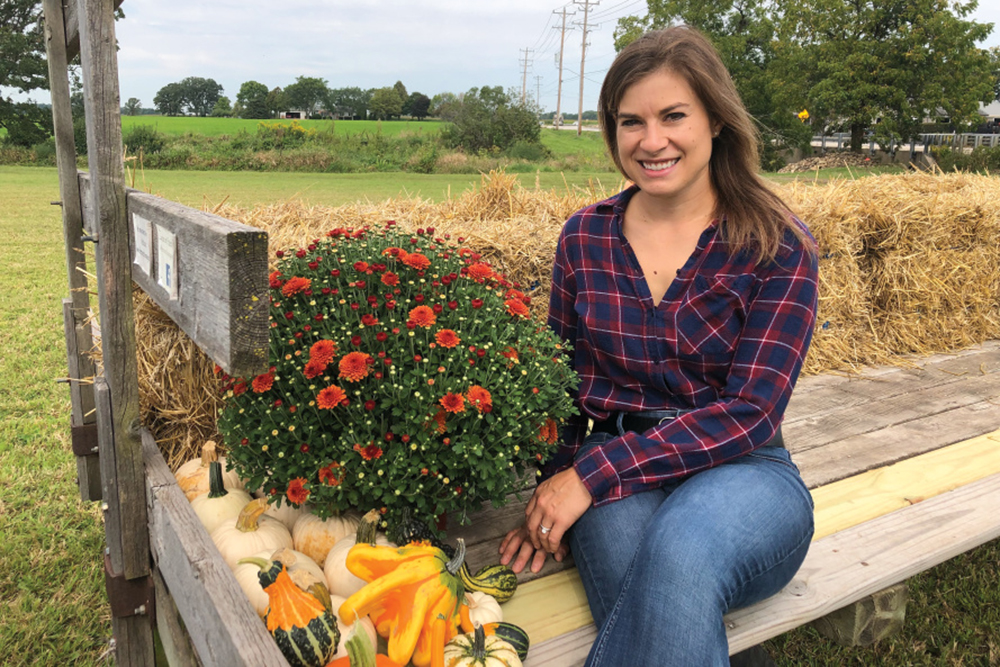 Carolyn Brummel sitting on a wagon with pumpkins and mums