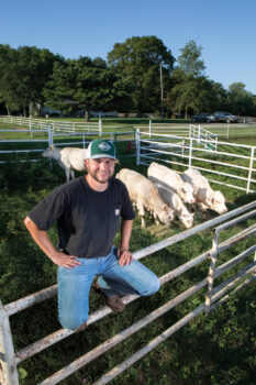 Sam Deisher sitting on the fence with cattle in the background