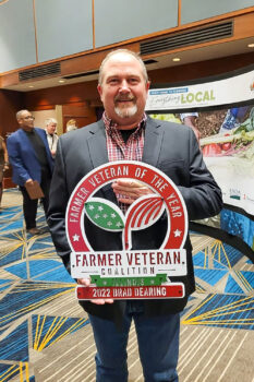 Brad Dearing holding a Farmers Veteran Coalition sign for Farmer Veteran of the Year