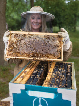 Hive with bees buzzing about with Amber Rutledge in the background