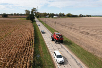 Farm equipment and cars on a road surrounded