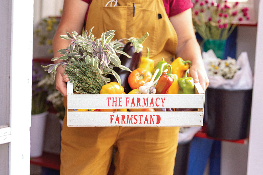 Pearl Carpenter holds a box with The Farmacy Farmstand painted on it field with produce
