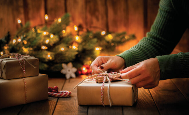 Up-close of a womans hands tying a bow around a Christmas package wrapped with brown paper