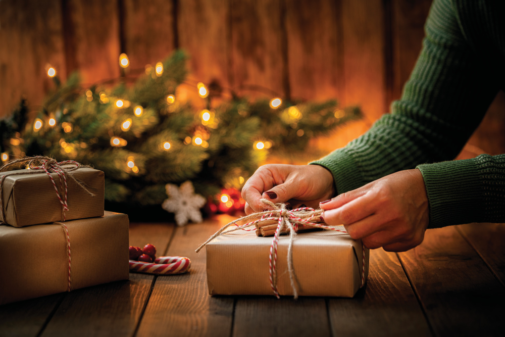 Up-close of a womans hands tying a bow around a Christmas package wrapped with brown paper