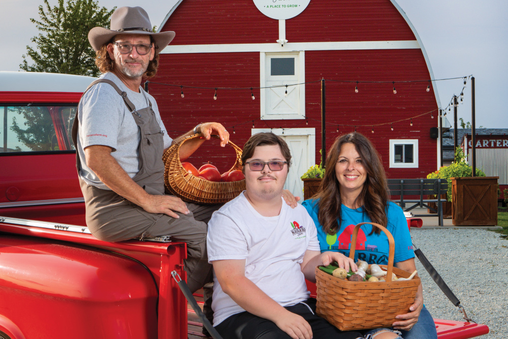 Damion, Sherri and Carter Navarro sitting in the bed of a red antique truck with a red barn in the background that has a Navarro Farm sign