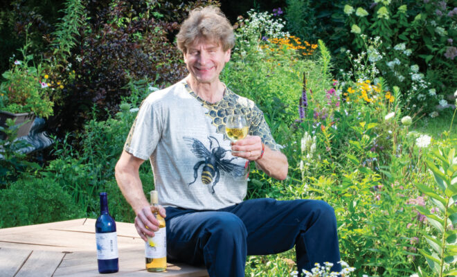Greg Fischer sitting in his pollinator garden with a glass of Wild Blossom Mead