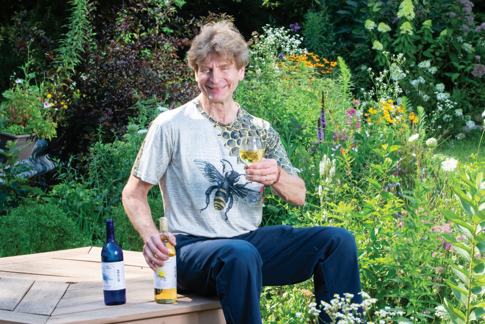 Greg Fischer sitting in his pollinator garden with a glass of Wild Blossom Mead