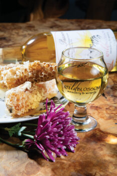 A glass of Wild Blossom Mead sitting next to flowers and honey comb