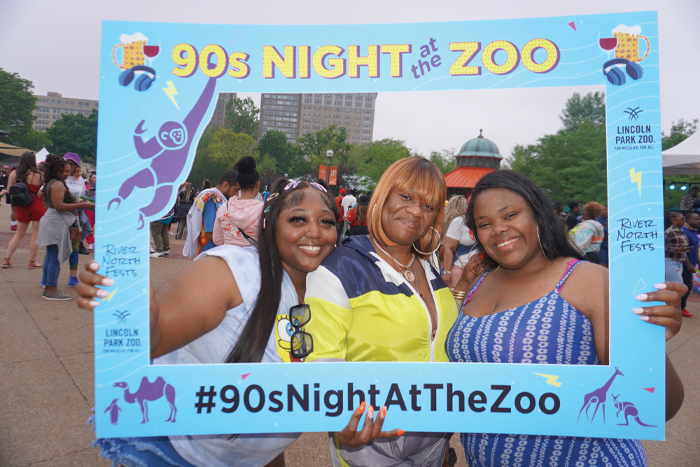 Three women pose with a photo frame for the Lincoln Park Zoo 21+ Nights