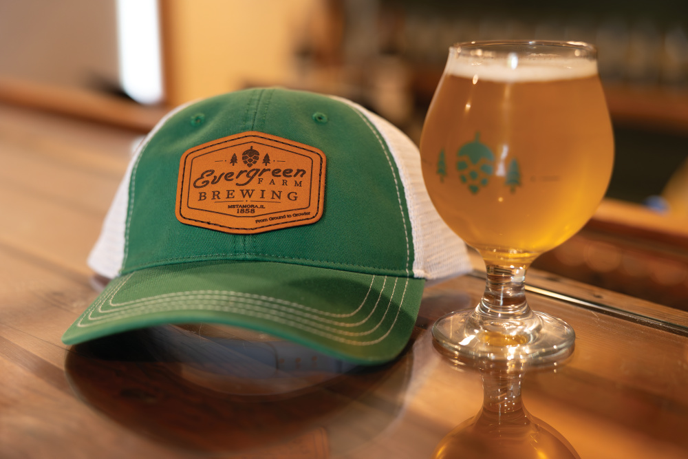 Evergreen Farm Brewing baseball hat sitting next to a glass of beer
