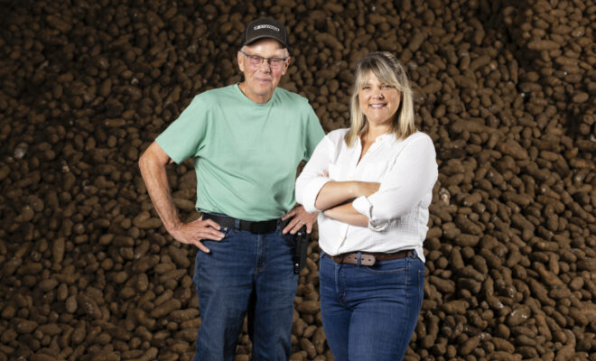 Tom Neumiller and Katie Neumiller-Floming standing in front of a large pile of potatoes at Neumiller Farms