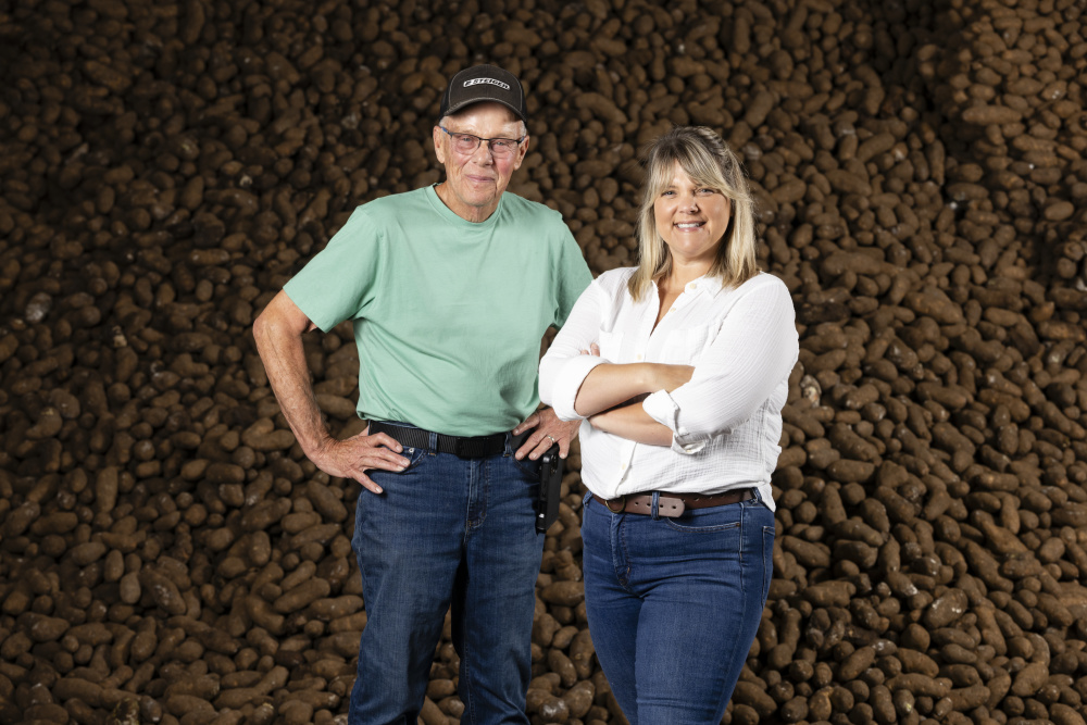 Tom Neumiller and Katie Neumiller-Floming standing in front of a large pile of potatoes at Neumiller Farms
