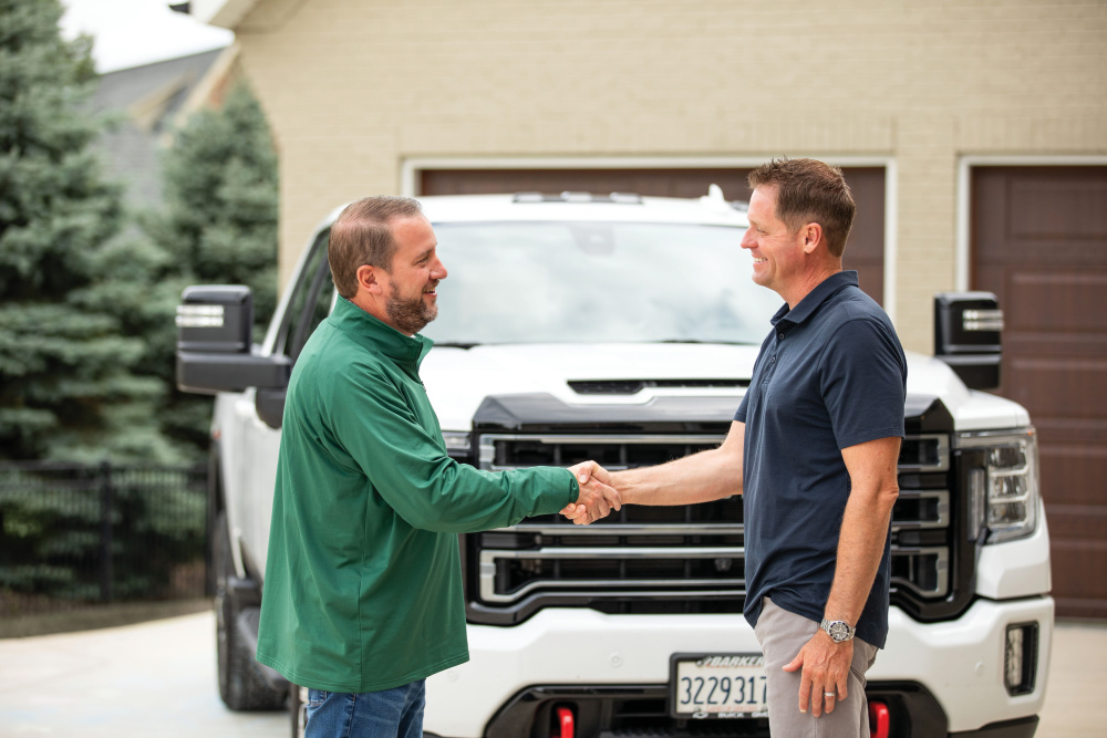 Two men shaking hands in front of a vehicle